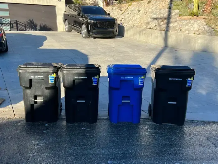 Four freshly cleaned carts at the curb, each with a small sticker on the lid
