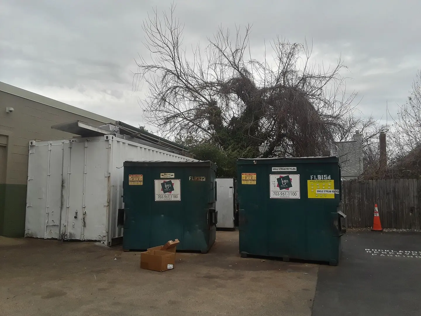 Two green front-load dumpsters with hauler stickers on the asphalt behind a business