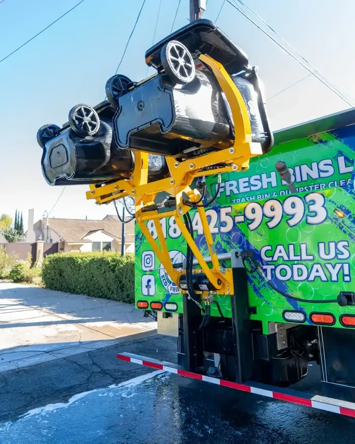 A yellow hydraulic lift on the back of a green truck holding two black carts upside down